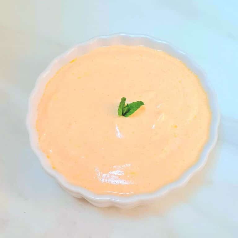 white bowl of spicy yogurt sauce with a mint sprig.