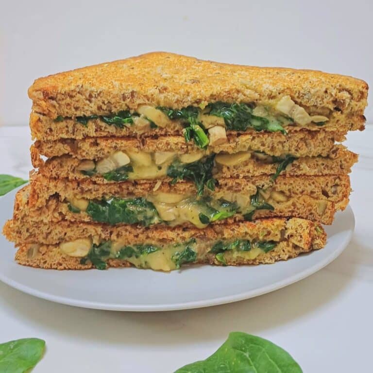 spinach mushroom sandwich on a plate placed on marble along with a few spinach leaves.