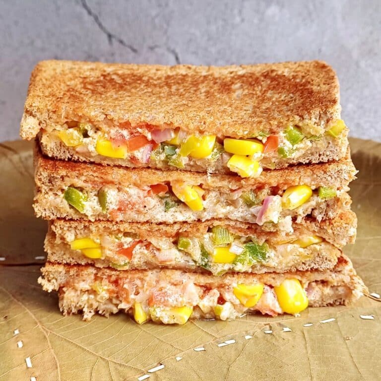 corn capsicum sandwich stacked on green leaf plate.