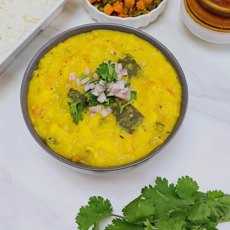 zucchini dal in black bowl placed on marble along with a bowl of rice, carrot dish and pickle bowl.