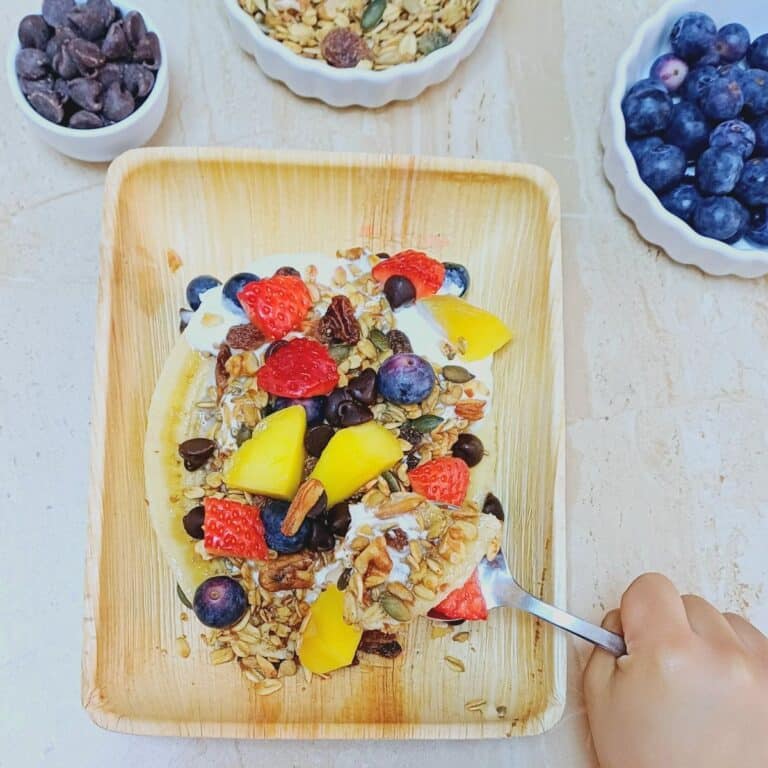 child holding the spoonful of banana split breakfast on top of the plate.