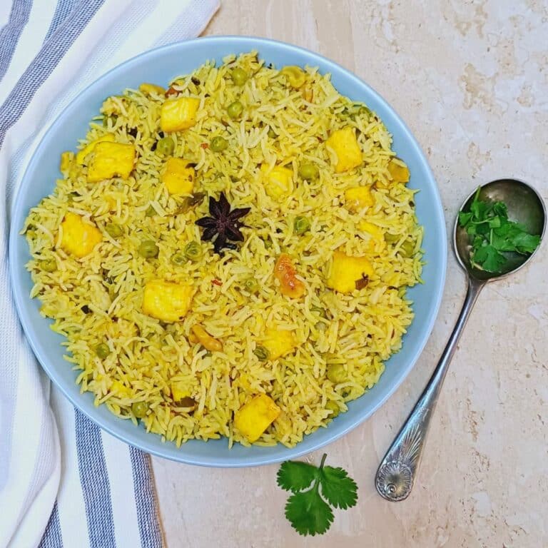 blue bowl filled with matar paneer pulao placed on granite along with a spoon and napkin.