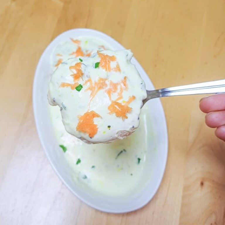 holding a spoon of curd vada on top of plate placed on wooden table.