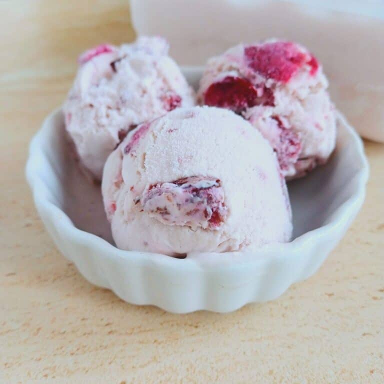 white bowl of 3 scoops cherry ice cream placed on a tile.