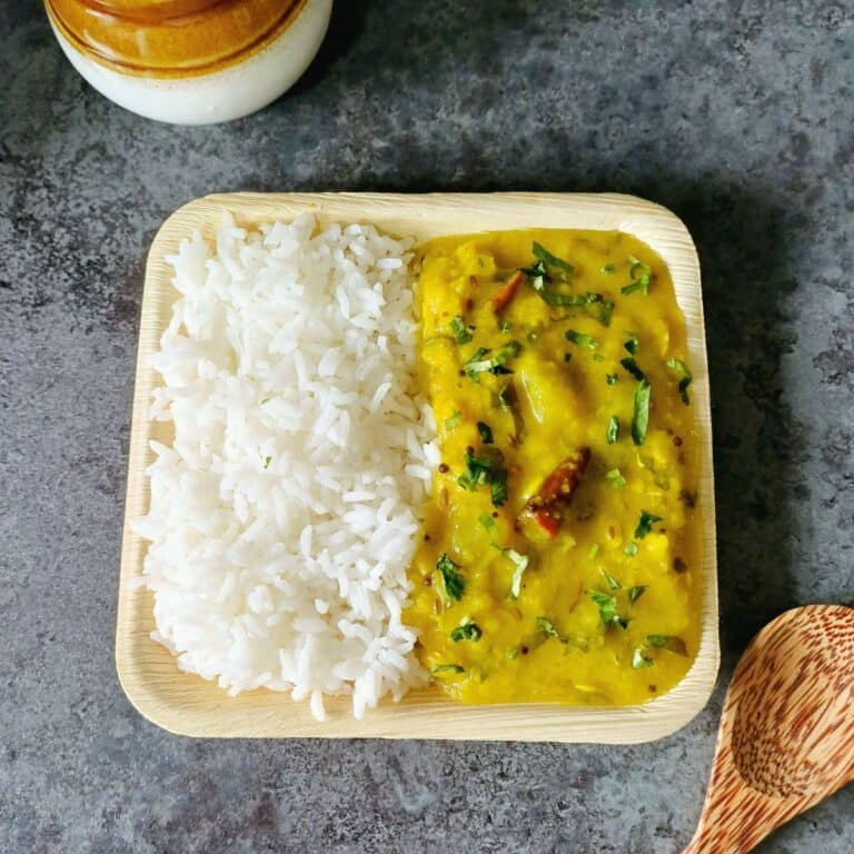 plate filled with rice and raw mango dal placed on granite along with a spoon and pickle bowl.