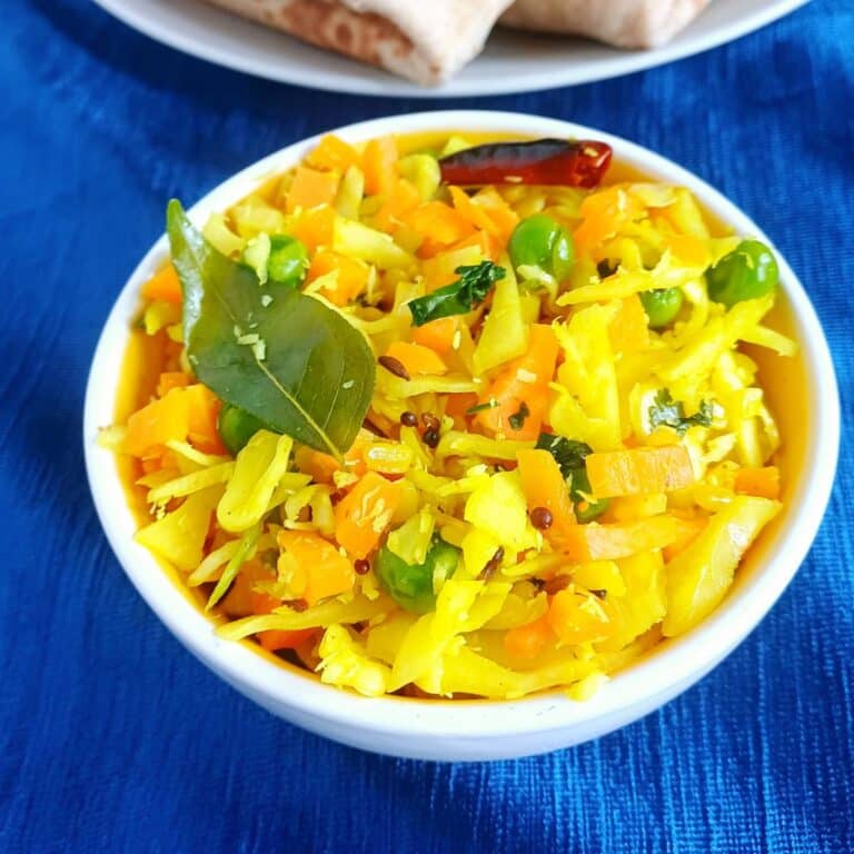 white bowl of cabbage carrot peas poriyal placed on blue cloth.
