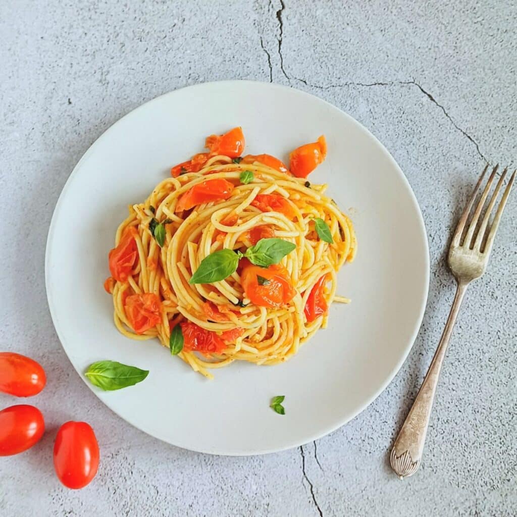 grey plate of tomato basil pasta placed on a tile along with a fork.
