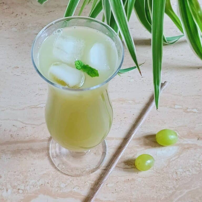 tall glass of green grape juice placed on a tile along with a straw.