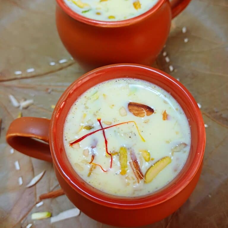 2 clay cups of kesar doodh placed on green leaf.