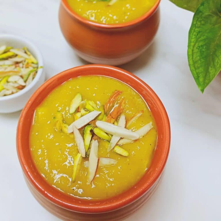 2 pots of mango phirni placed on marble along with a pinch bowl of nuts.