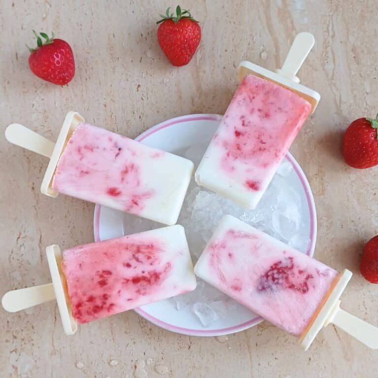 4 strawberry yogurt popsicles on white plate placed on a granite along with fresh strawberries.