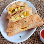 cut paneer puff placed on a plate of puffs.