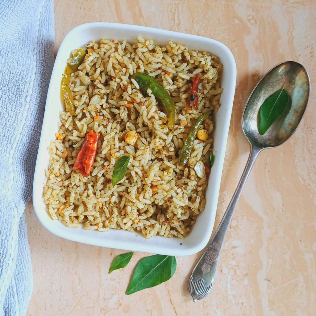 curry leaves masala rice in a rectangle white bowl placed on tile.