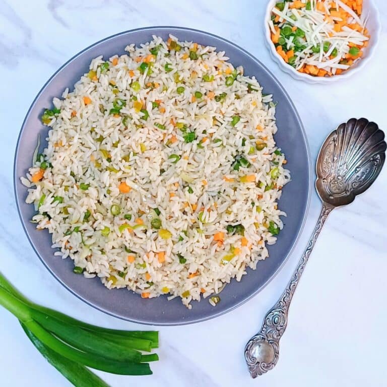 grey bowl of vegetable fried rice placed on marble along with a spoon and a bowl of chopped vegetables.