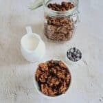 chocolate peanut butter granola placed on a tile along with a mug of milk and a bowl of chocolate chips
