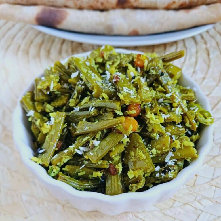 chikkudu kaya fry in a white bowl placed on a mat with a plate of chapatis.