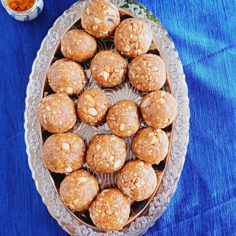 silver oval tray filled with peanut laddos placed on blue cloth.