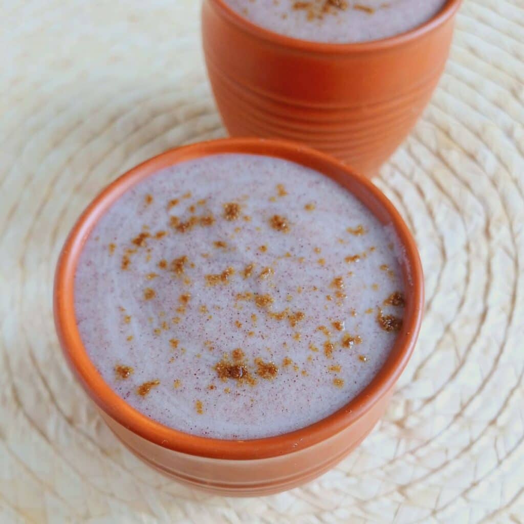 glass of ragi porridge placed on wooden placemat.