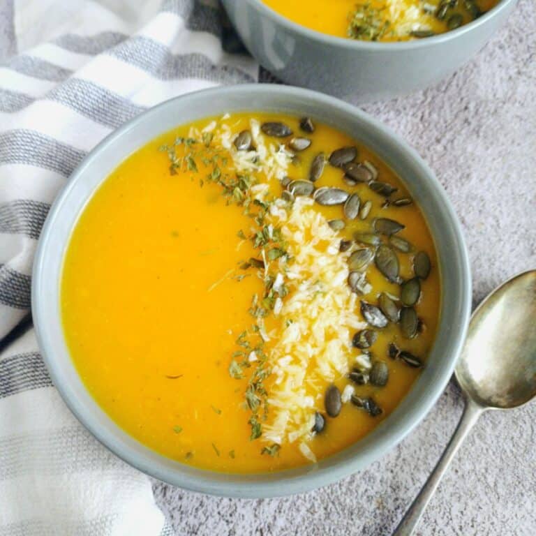 grey bowl of sweet potato soup with pumpkin seeds, desiccated coconut and herb toppings.