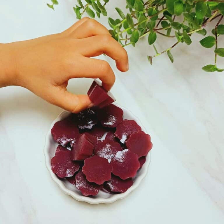 child picking up a black grape gummy from a bowl filled with gummies.
