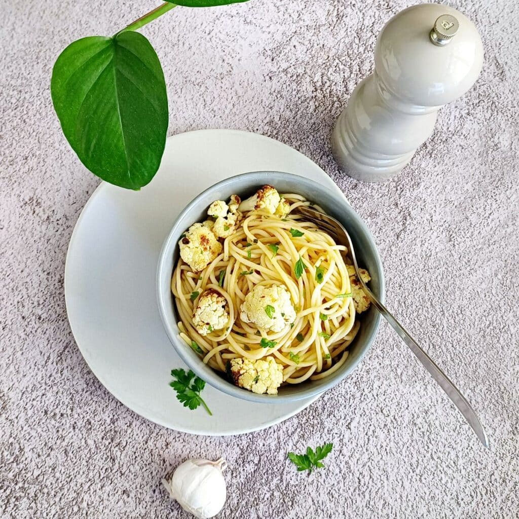bowl of roasted cauliflower pasta in a plate placed on grey backdrop along with a fork.