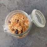 homemade crunchy granola in a glass jar placed on black tile.