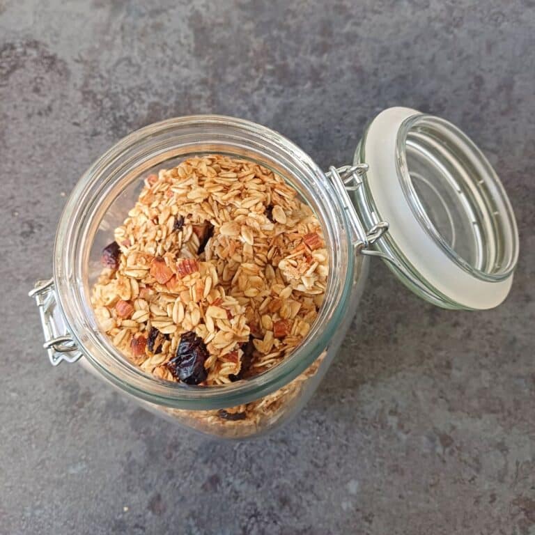homemade crunchy granola in a glass jar placed on black tile.