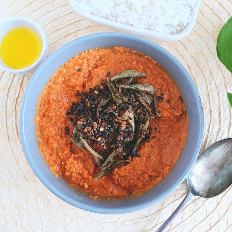 grey bowl of kandi pachadi with tempering placed on wooden placemat along with a spoon and bowl of rice and ghee.