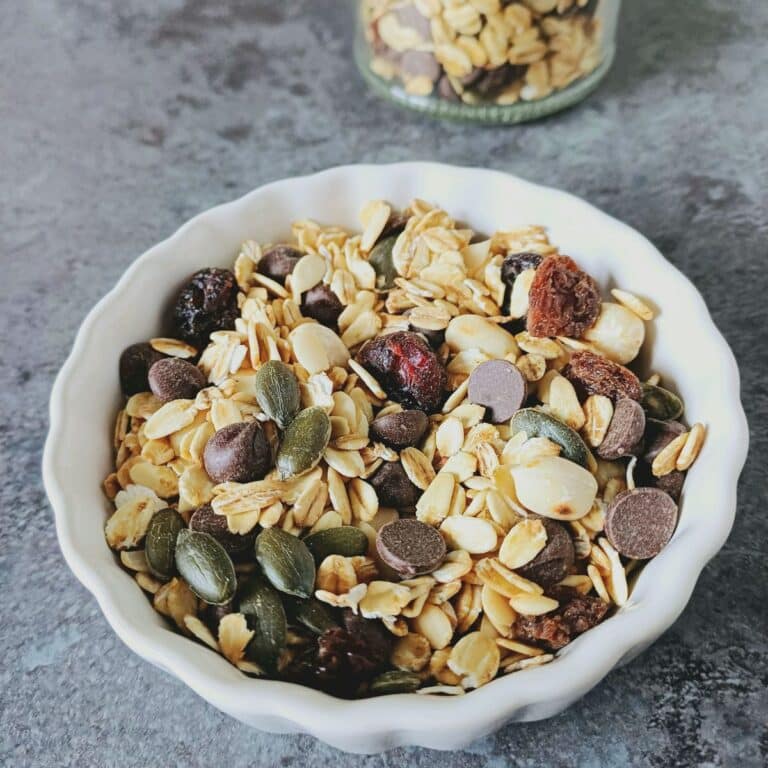 white bowl of healthy trail mix placed on black tile.
