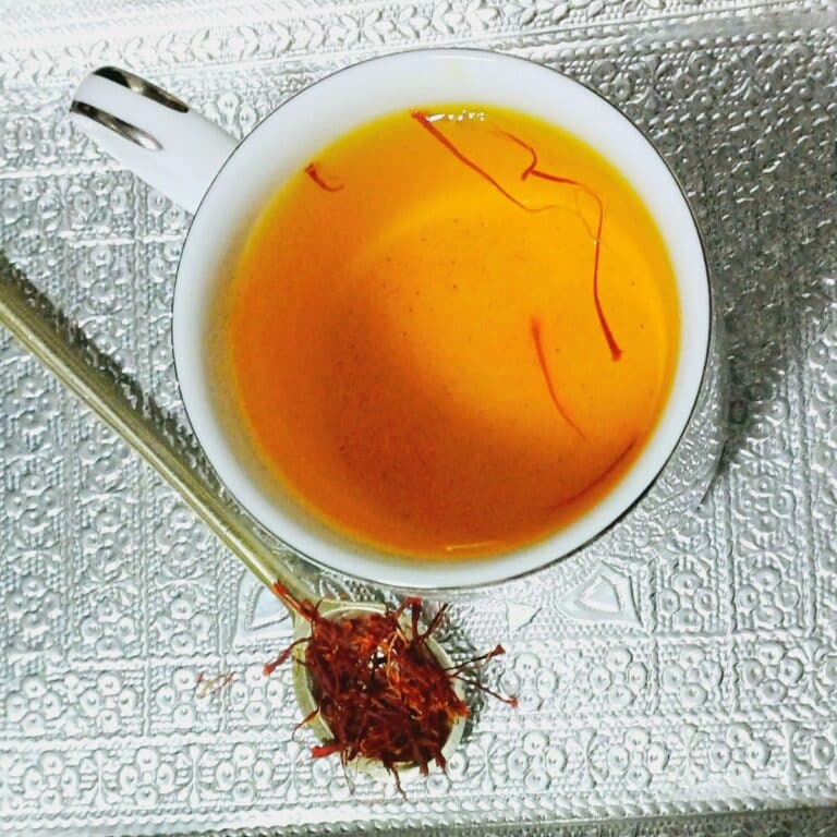 cup of saffron tea placed on silver plate along with a spoon of saffron threads.