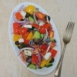 white plate of greek vegetable salad placed on granite along with a fork.