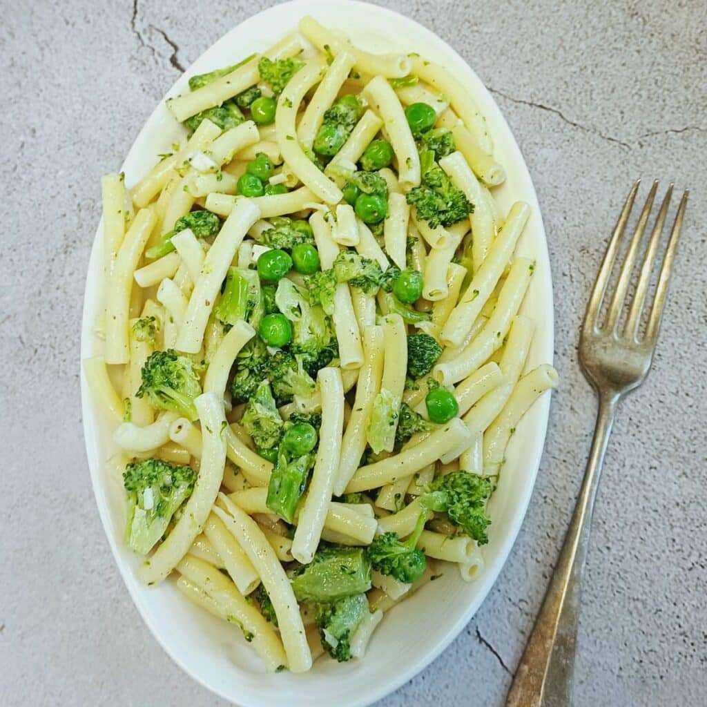 white plate of broccoli peas pasta on blue tile.