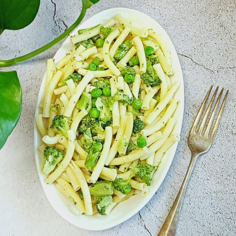 white plate of broccoli peas pasta on blue tile along with fork