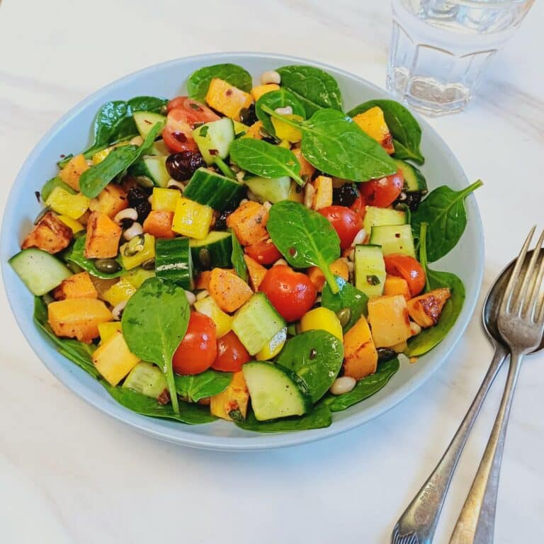 blue bowl of roasted butternut squash black eyed peas salad placed on marble along with spoon and fork.