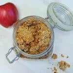 glass jar of apple granola placed on marble along with apple.