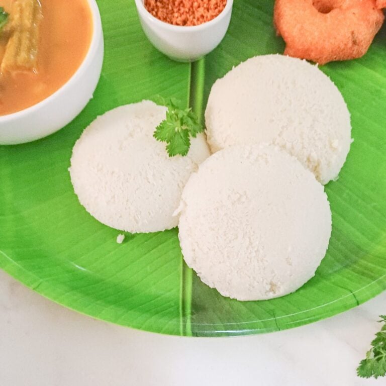 3 rice idlis, vada and sambar on a green plate.