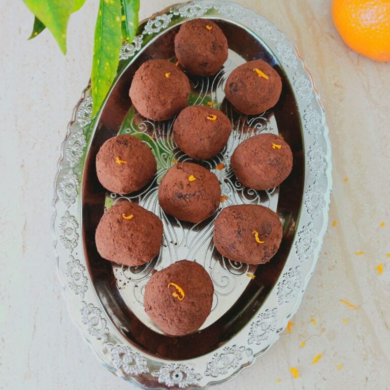 orange cocoa balls on silver plate placed on a tile along with a orange.