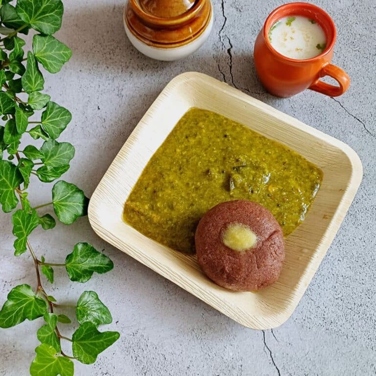 ragi mudde with dal in a brown plate placed on a blue tile along with glass of lassi and pickle bowl.