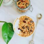 bowl of yogurt topped with granola placed on a marble along with a spoon.
