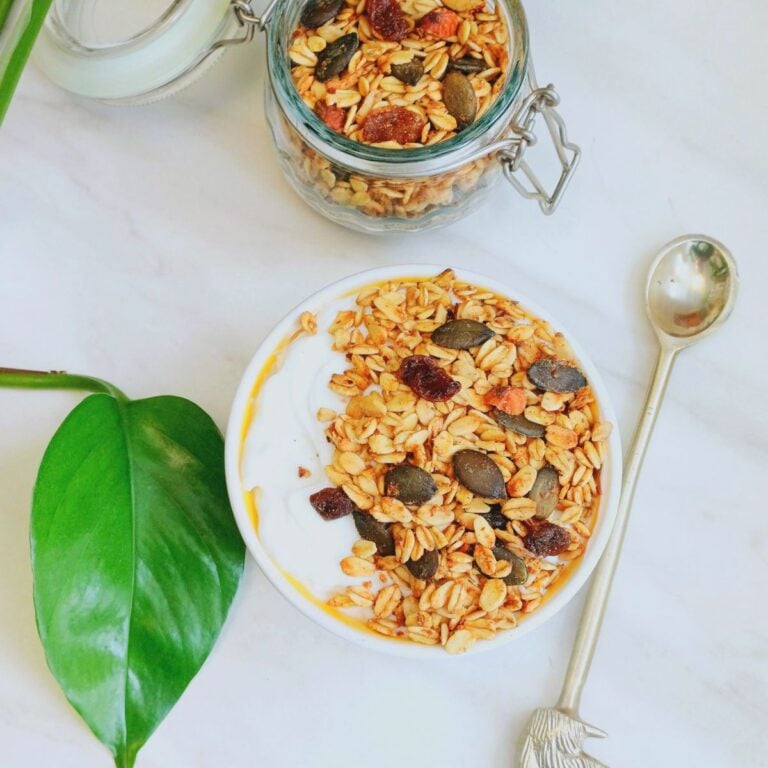bowl of yogurt topped with granola placed on a marble along with a spoon.