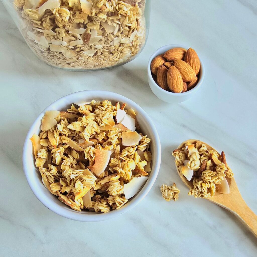 coconut shell filled with granola placed on granite along with a few almonds and coconut flakes.