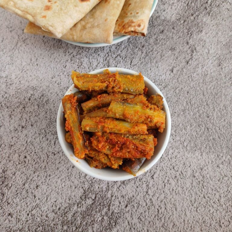 spicy eggplant stir fry in a white bowl on grey backdrop along with chapatis in a plate.