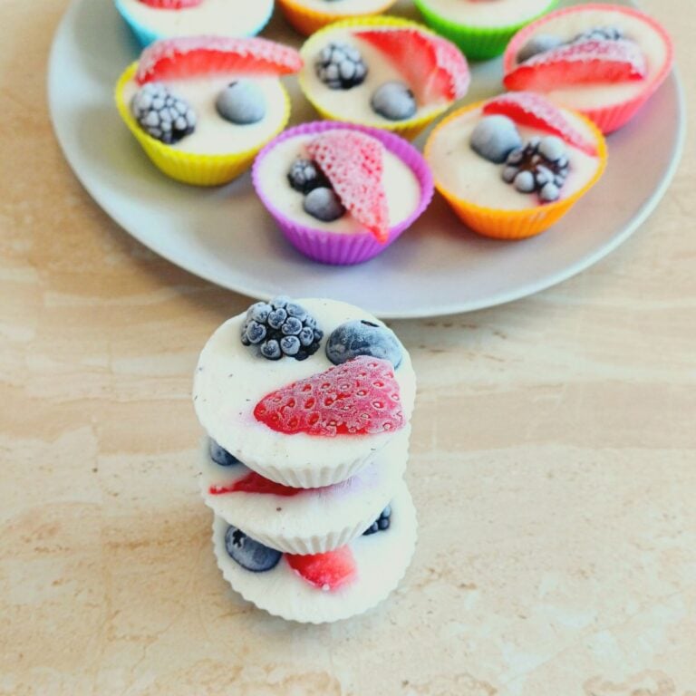 three stacked frozen mixed berry yogurt bites placed on a tile along with a grey plate of more frozen bites.