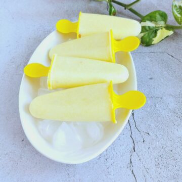 pineapple popsicles on top of ice cubes on a white plate.