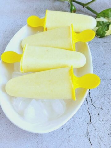 pineapple popsicles on top of ice cubes on a white plate.