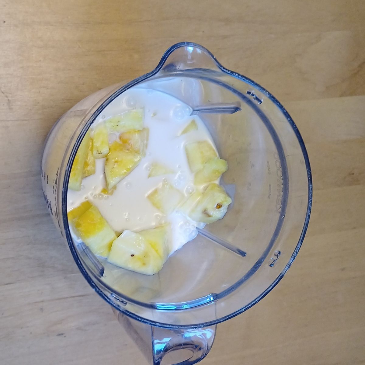 blender jar half filled with pineapple chunks and milk