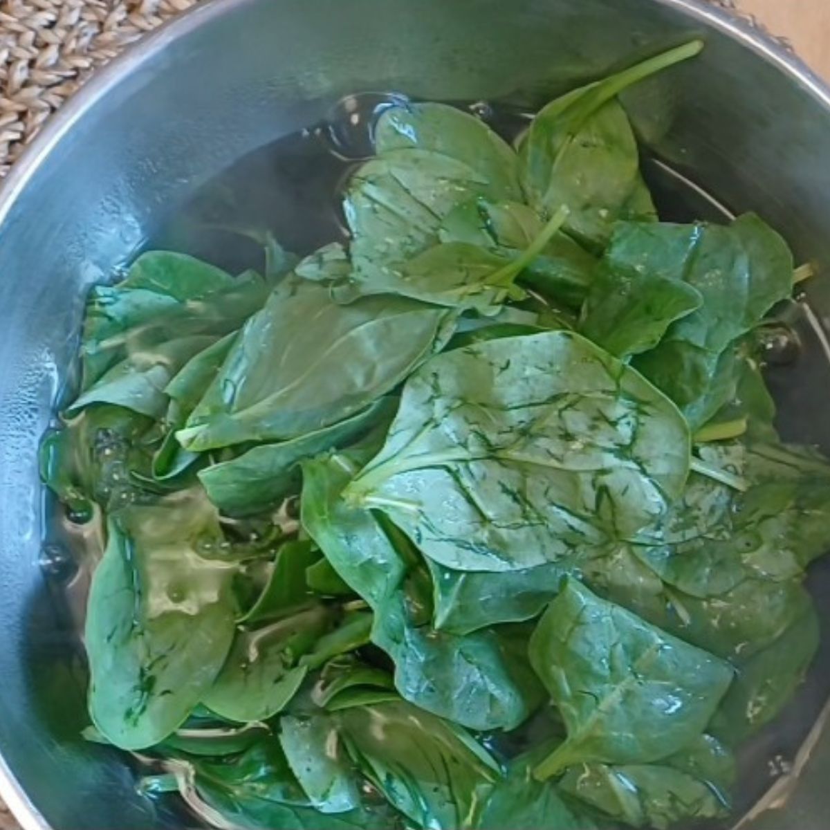 fresh spinach leaves in a steel bowl of water.