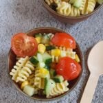 wooden bowl of kid friendly pasta salad placed on a tile along with a wooden spoon.