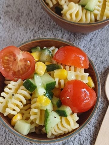 wooden bowl of kid friendly pasta salad placed on a tile along with a wooden spoon.