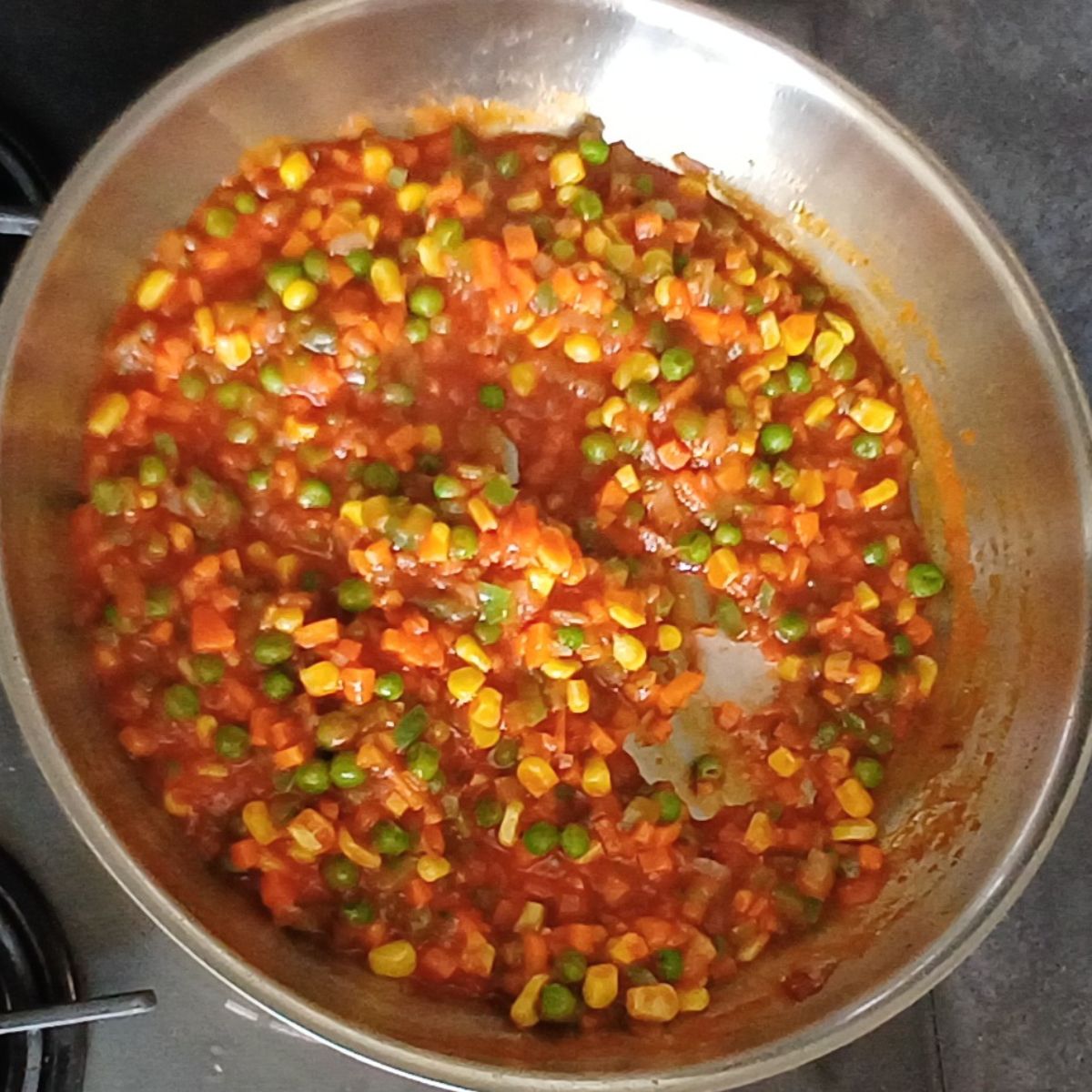 cooking vegetables and red sauce in a steel pan.